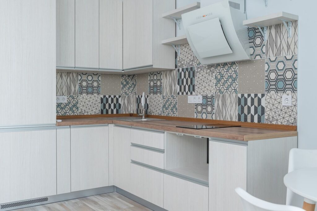 Interior of contemporary kitchen with white cabinets and wooden counter near ornamental tile on wall and modern appliances in apartment